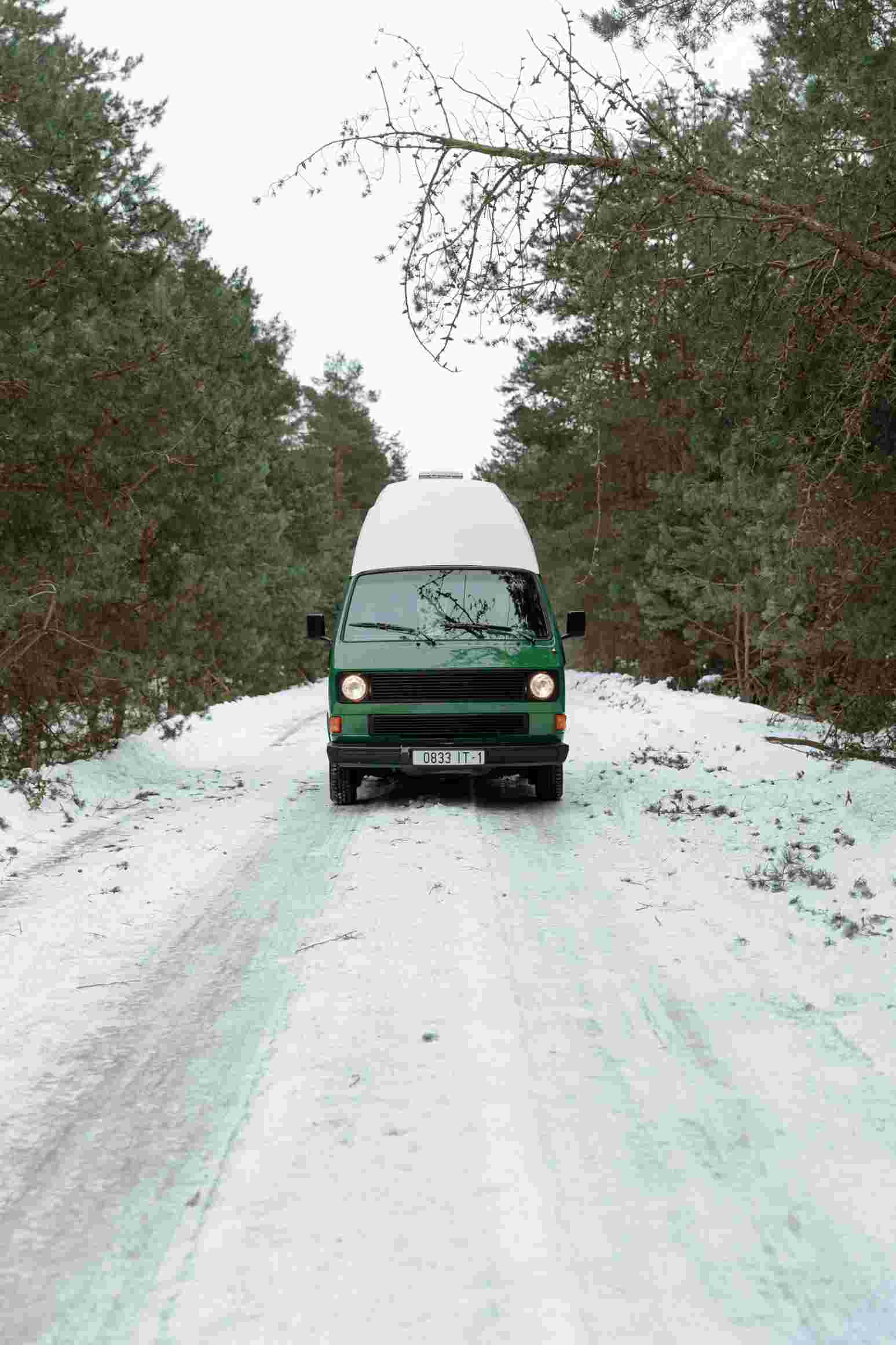 A campervan travels on a snowy forest road, showcasing a serene winter landscape ideal for adventure travel.