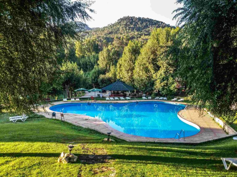 Relax at a luxury resort pool surrounded by lush greenery and scenic hills in Jaén, Spain.